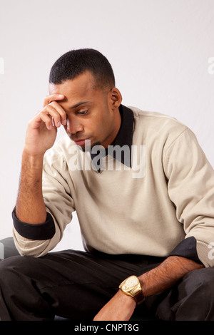 Giovane uomo nero in marrone maglione, seduta con la mano sulla fronte, pensando pensieri gravi Foto Stock