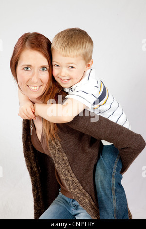 Piuttosto redheaded madre dando il suo biondo figlio di fare un giro sulla sua schiena, entrambi sorridente con la gioia del rapporto Foto Stock