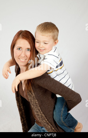 Piuttosto redheaded madre dando il suo biondo figlio di fare un giro sulla sua schiena, entrambi sorridente con la gioia del rapporto Foto Stock