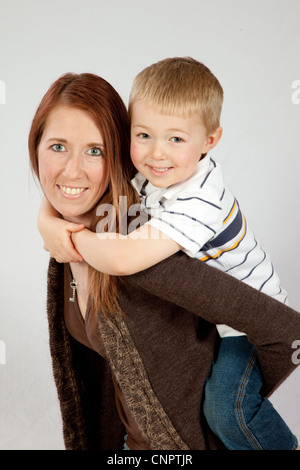 Piuttosto redheaded madre dando il suo biondo figlio di fare un giro sulla sua schiena, entrambi sorridente con la gioia del rapporto Foto Stock