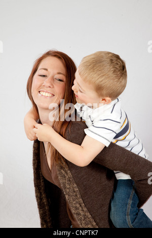 Piuttosto redheaded madre dando il suo biondo figlio di fare un giro sulla sua schiena, entrambi sorridente con la gioia del rapporto Foto Stock