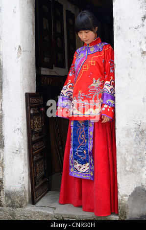 Giovane sposa indossa il suo red abito da sposa alla porta di un villaggio di hongcun edificio repubblica popolare cinese Foto Stock