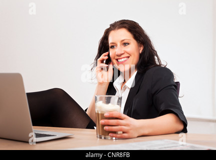 Ritratto di un giovane dirigente con un drink su una mano a parlare al telefono Foto Stock