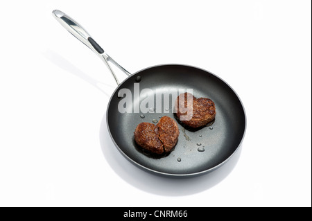 Due a forma di cuore hamburger di manzo in una padella, uno rotto Foto Stock