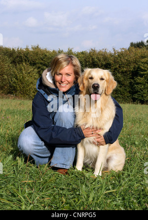 Golden Retriever (Canis lupus f. familiaris), giovane donna inginocchiata sul prato, abbracciando un cane maschio Foto Stock