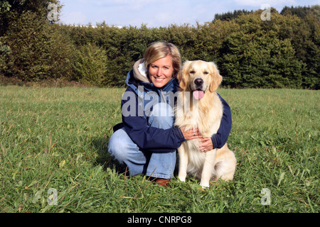 Golden Retriever (Canis lupus f. familiaris), giovane donna inginocchiata sul prato, abbracciando un cane maschio Foto Stock