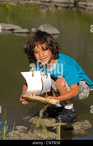 Ragazzo felicemente a sorridere mentre lancia il suo self-made barca giocattolo, Francia Foto Stock