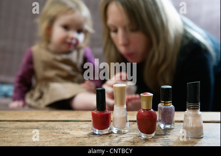 Le bottiglie di smalto per unghie, madre soffiando sul giovane figlia di dita in background Foto Stock