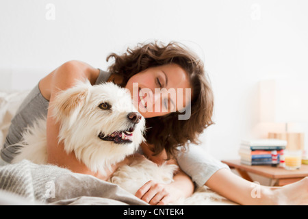 Donna sorridente petting cane nel letto Foto Stock