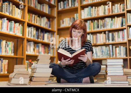 Studente nella pila di libri in biblioteca Foto Stock