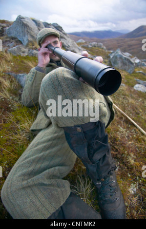 Stalker giacente in erba su un pendio di montagna guardando in giù in una valle fluviale attraverso un telescopio, Regno Unito, Scozia, Sutherland, Alladale deserto riserva Foto Stock