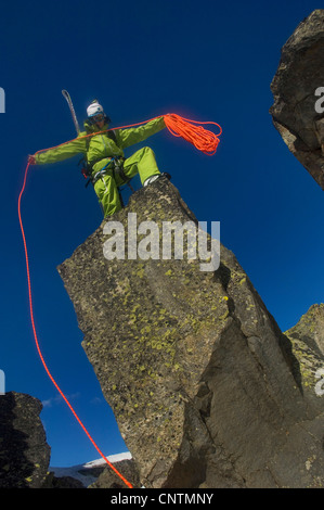 Alpinista di sci in piedi su una roccia e buttare giù un rosso corda di arrampicata, Francia, Alpi Foto Stock