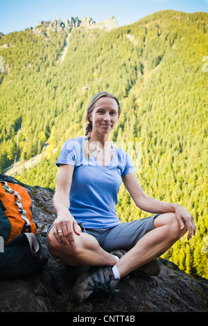 Una donna escursionista seduto sul bordo di una scogliera rocciosa, poco si Trail, Washington, Stati Uniti d'America. Foto Stock