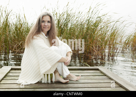 Donna anziana seduta sul dock in legno Foto Stock