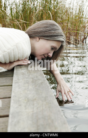 Donna anziana immergendo le dita nel lago Foto Stock