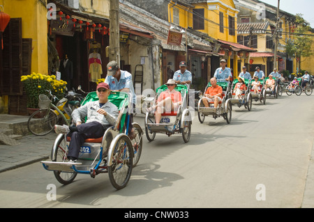 Orizzontale vista umoristico di turisti sul ciclo-rickshaws o cyclo cavalcando attraverso la antica città di Hoi An, Vietnam. Foto Stock