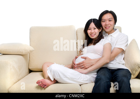 Coppia asiatica. Il marito e 8 mesi di gravidanza moglie seduta sul divano. Foto Stock