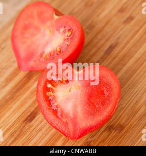 Dire che con i pomodori - a forma di cuore il pomodoro tagliato a metà su un tagliere di legno Foto Stock