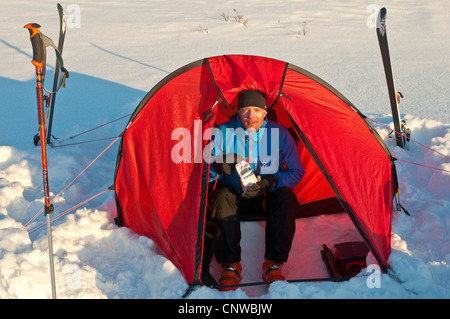 Sciatore seduto nel suo accampamento mangiare liofilizzato cibo, Svezia, la Lapponia Norrbotten, Sarek National Park Foto Stock