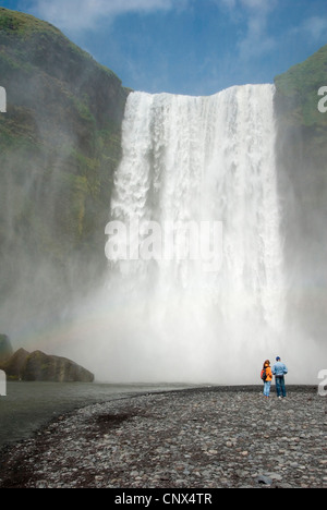 Due visitatori presso la riva del Skoga di fronte all'impressionante cascata Skogafoss, Islanda, Skogar Foto Stock