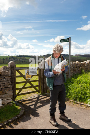 Un viandante la lettura di una mappa accanto a un cancello sul D'arcy Dalton sentiero nel villaggio Costwold di Great Barrington, Gloucestershire Foto Stock