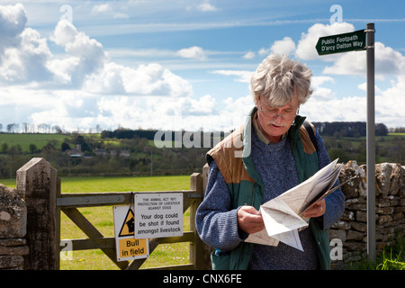 Un viandante la lettura di una mappa accanto a un cancello sul D'arcy Dalton sentiero nel villaggio Costwold di Great Barrington, Gloucestershire Foto Stock