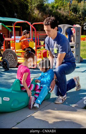 Un giovane membro del personale aiuta i ciechi e storpi i bambini utilizzano il parco giochi presso la Tenda per bambini Centro di apprendimento. Foto Stock