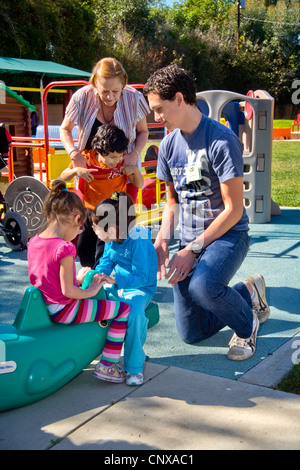 Giovani e vecchi membri dello staff aiutare i ciechi e storpi i bambini utilizzano il parco giochi presso la Tenda per bambini Centro di apprendimento. Foto Stock