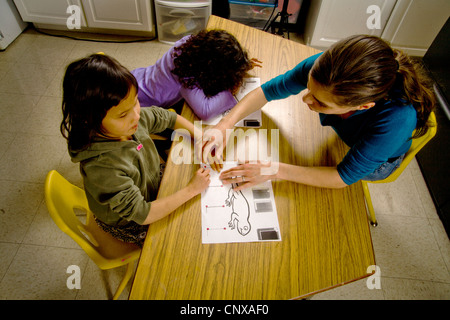 Un insegnante guida un bambino non vedente le mani sopra il contorno di una lucertola in rilievo in una speciale ha bisogno di scrittura di classe. Foto Stock
