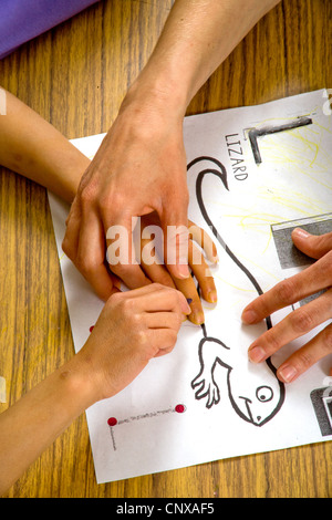 Un insegnante guida un bambino non vedente le mani sopra il contorno di una lucertola in rilievo in una speciale ha bisogno di scrittura di classe. Foto Stock