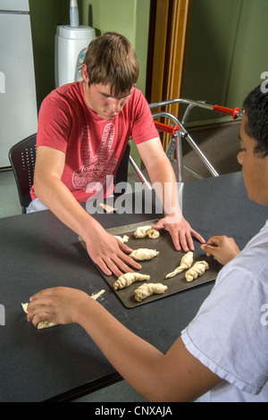 Un insegnante aiuta un handicap ipovedenti teenager fare rotoli da toccare dalla pasta preparata in una classe di cucina. Foto Stock