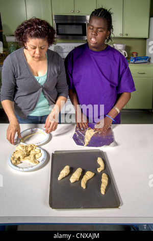 Assistito da un insegnante, un cieco afro-americano di preteen girl produce rotoli da toccare dalla pasta preparata in una classe di cucina. Foto Stock