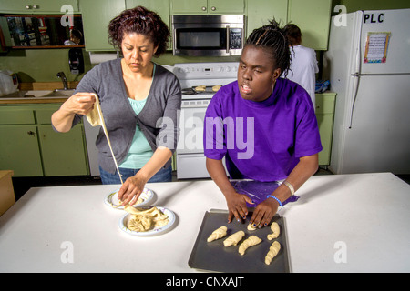 Assistito da un insegnante, un cieco afro-americano di preteen girl produce rotoli da toccare dalla pasta preparata in una classe di cucina. Foto Stock