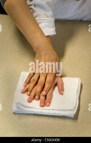 Un insegnante del lato guida la mano di un cieco teen apprendimento dello studente per piegare un asciugamano da toccare in un abilità pratiche di classe. Foto Stock