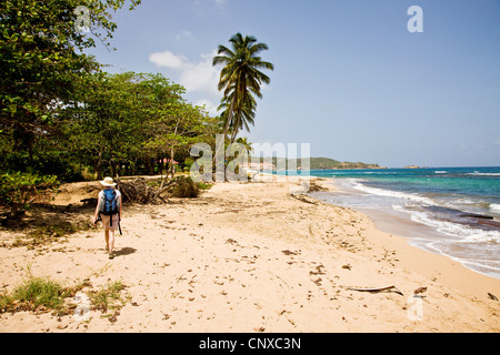 Una giovane donna cammina lungo la spiaggia sabbiosa a Woodford Hill Bay sulla costa est della Dominica West Indies Foto Stock