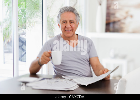 Un allegro uomo senior la lettura della carta e di bere il caffè Foto Stock