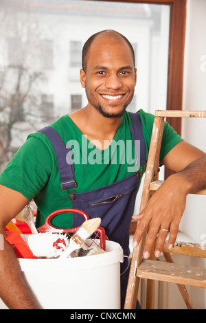 Un uomo con un secchio di vernice forniture appoggiato su di una scala a pioli Foto Stock