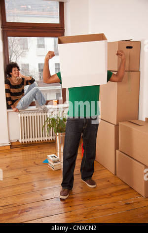 Un uomo con una scatola sulla sua testa flettendo i suoi muscoli mentre Donna Orologi Foto Stock