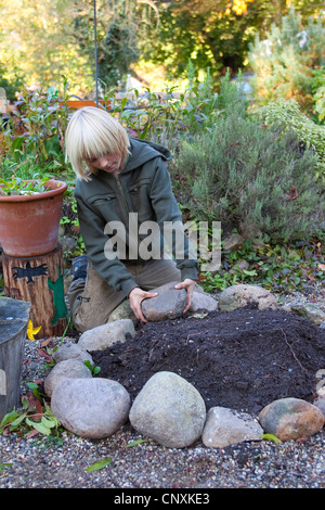 Ragazzo la costruzione di una spirale di erbe in un giardino, Germania Foto Stock