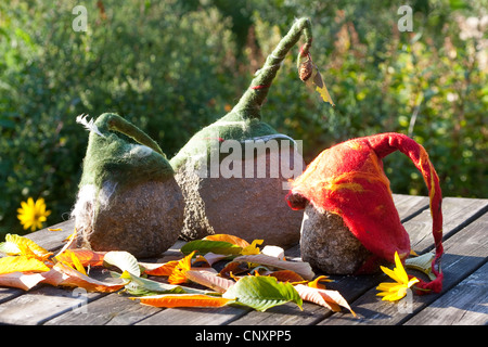 "Feltro stone troll' che serve come giardino decorazione: tre pietre naturali dotati di cappelli di feltro di lana in piedi a fianco a fianco su un tavolo da giardino, Germania Foto Stock