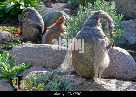 "Feltro stone troll' che serve come giardino decorazione: tre pietre naturali dotati di cappelli di feltro di lana sono in piedi a fianco a fianco in un letto di fiori, Germania Foto Stock