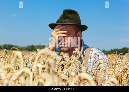 Frustrati agricoltore seduto nella sua coppia campo di grano tenendo una mano davanti al suo volto, Germania Foto Stock