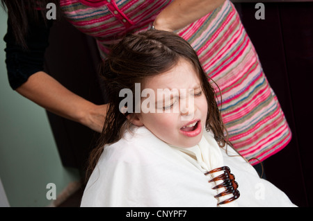 Bambina di cinque anni avente taglio capelli da sua madre proteste come capelli arruffati viene tirato. Foto Stock