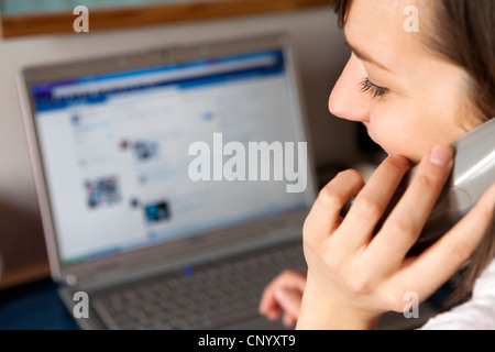 Una donna al telefono di fronte al computer,facebook Foto Stock