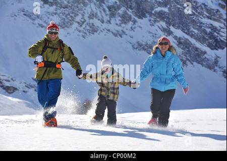 Famiglia in vacanza invernale felicemente a piedi attraverso un innevato paesaggio di montagna mano nella mano con le racchette da neve, Francia Foto Stock