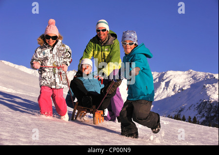 Madre seduto su una slitta avente fun trainato da suo marito e i suoi due figli, Francia Foto Stock