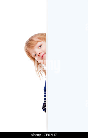 Curioso ragazzo con lunghi capelli biondi che spuntavano da dietro un pannello bianco cercando Foto Stock