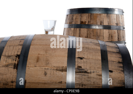 Bicchiere di whiskey su un barile di whiskey con una seconda canna in distanza, isolato su bianco e messa a fuoco selettiva su vetro Foto Stock