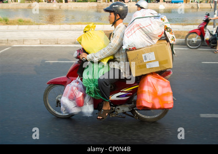 Chiudere orizzontale di un uomo alla guida di un ciclomotore sovraccaricato con scatole e buste, Vietnam. Foto Stock