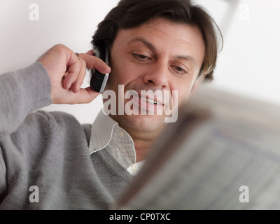 Ritratto di felice caucasian uomo adulto seduto sul divano, parlare con operatore sul cordless e controllare gli elenchi degli stock Foto Stock